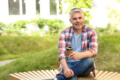 Photo of Handsome mature man with coffee on bench in park. Space for text