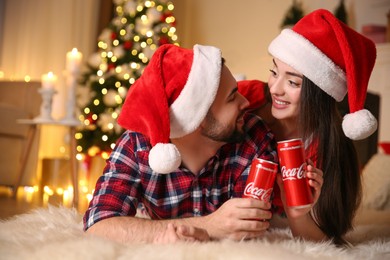 MYKOLAIV, UKRAINE - JANUARY 27, 2021: Young couple holding cans of Coca-Cola at home. Christmas atmosphere