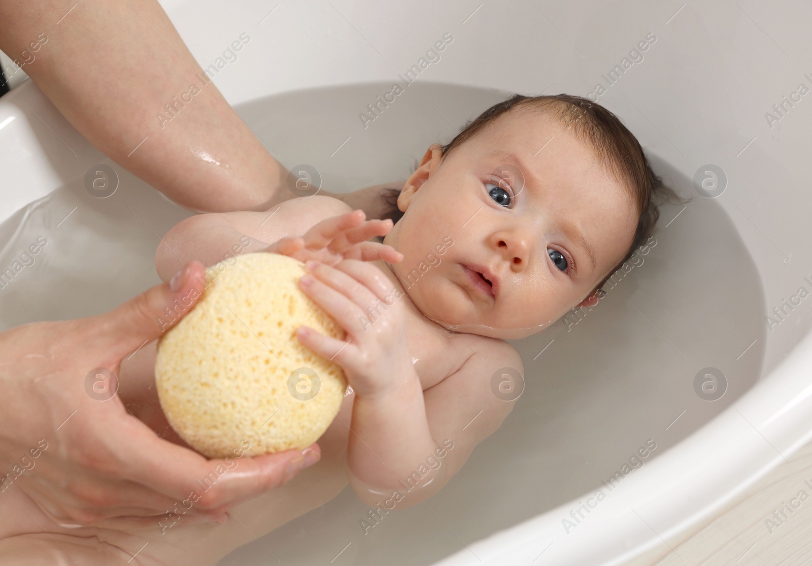 Photo of Mother bathing her little baby with sponge in bathtub, closeup