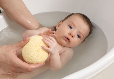 Mother bathing her little baby with sponge in bathtub, closeup