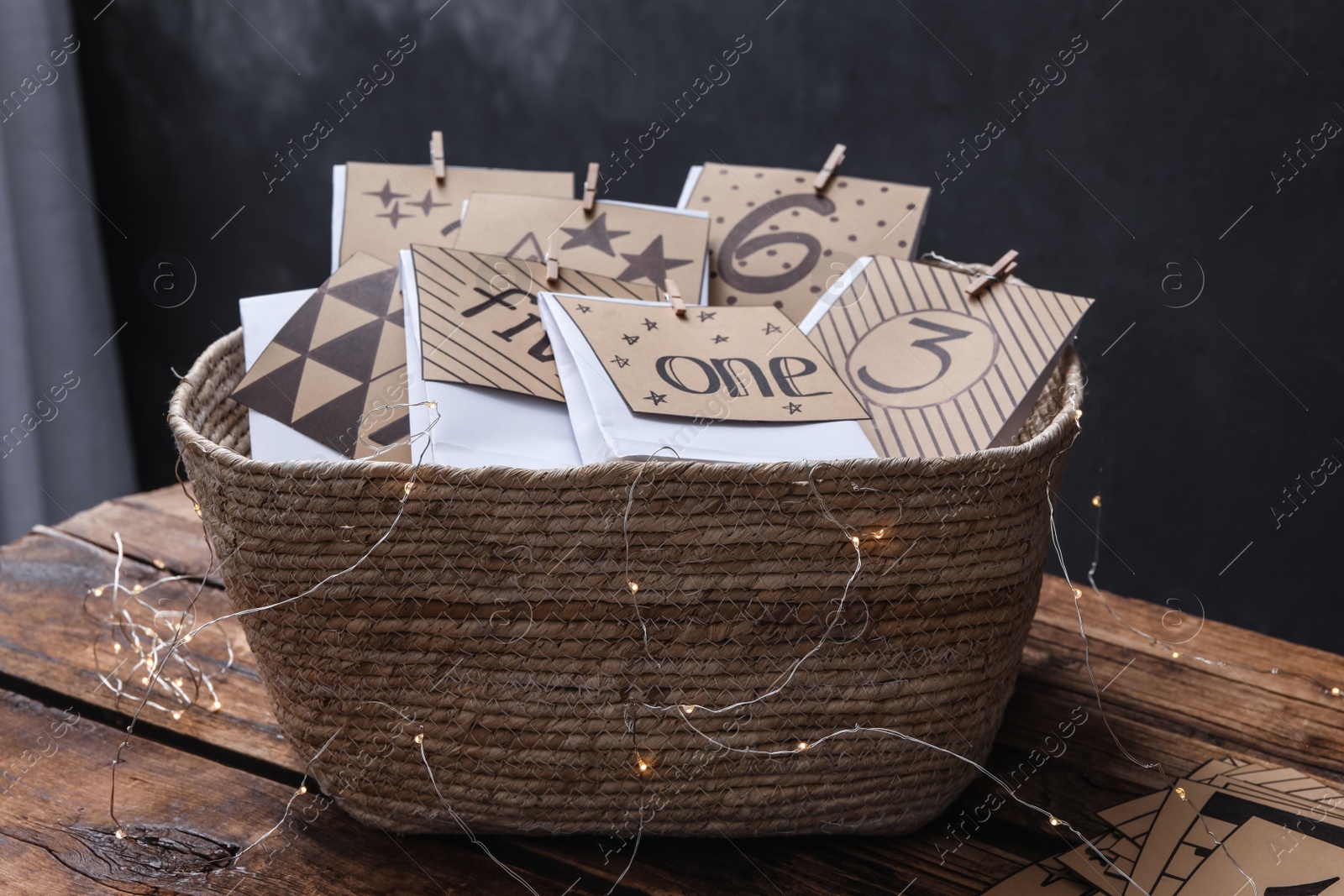 Photo of Many gift bags in wicker basket and garland on wooden table. Advent calendar