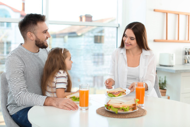 Photo of Happy family having breakfast with sandwiches at table in kitchen