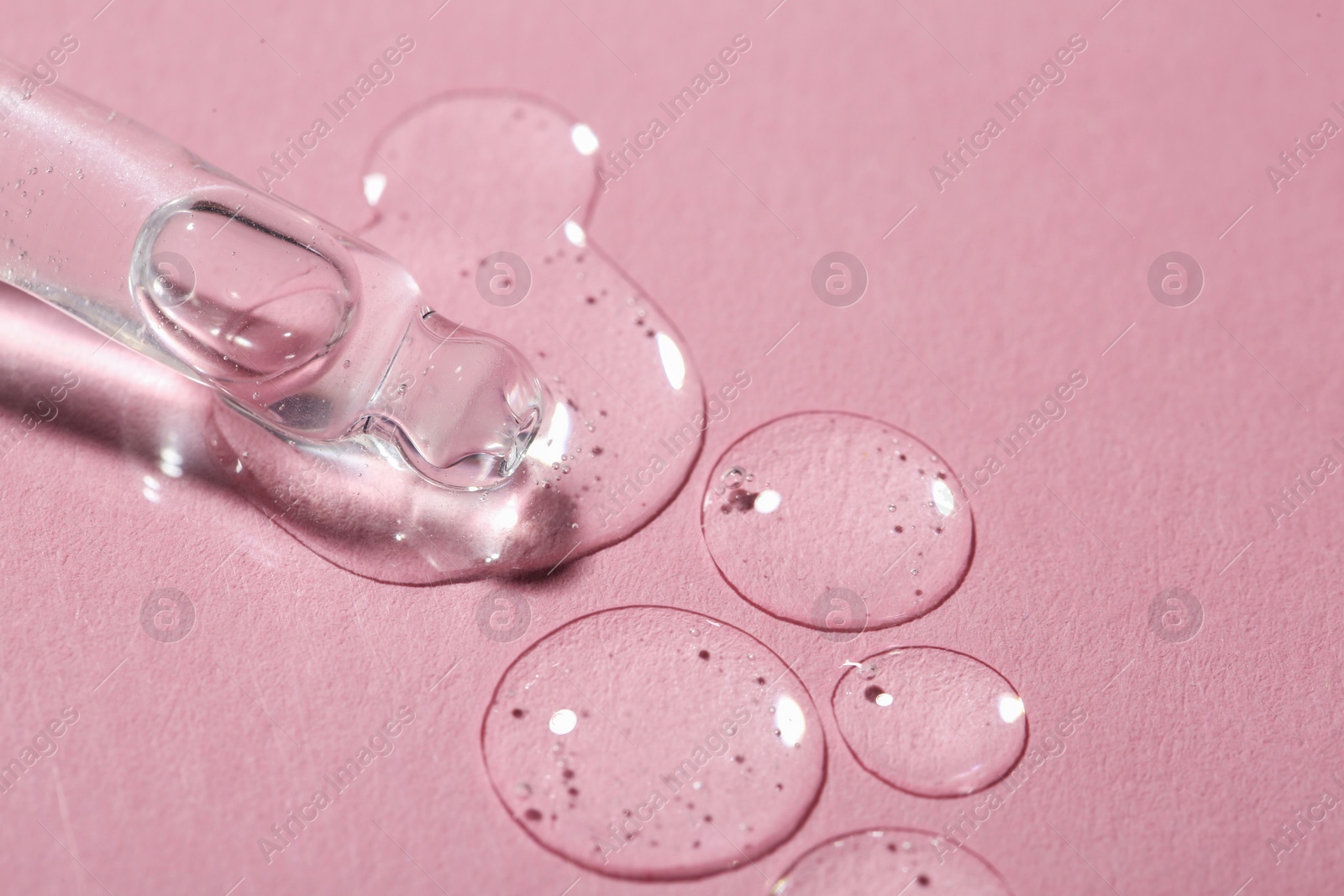 Photo of Dripping cosmetic serum from pipette onto pink background, macro view