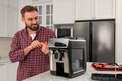 Photo of Man with screwdriver fixing coffee machine at table in kitchen