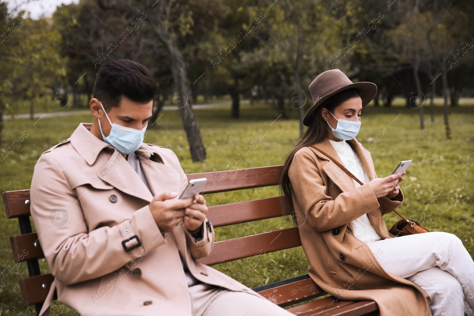 Photo of Man and woman using smartphones in park. Keeping social distance during coronavirus pandemic
