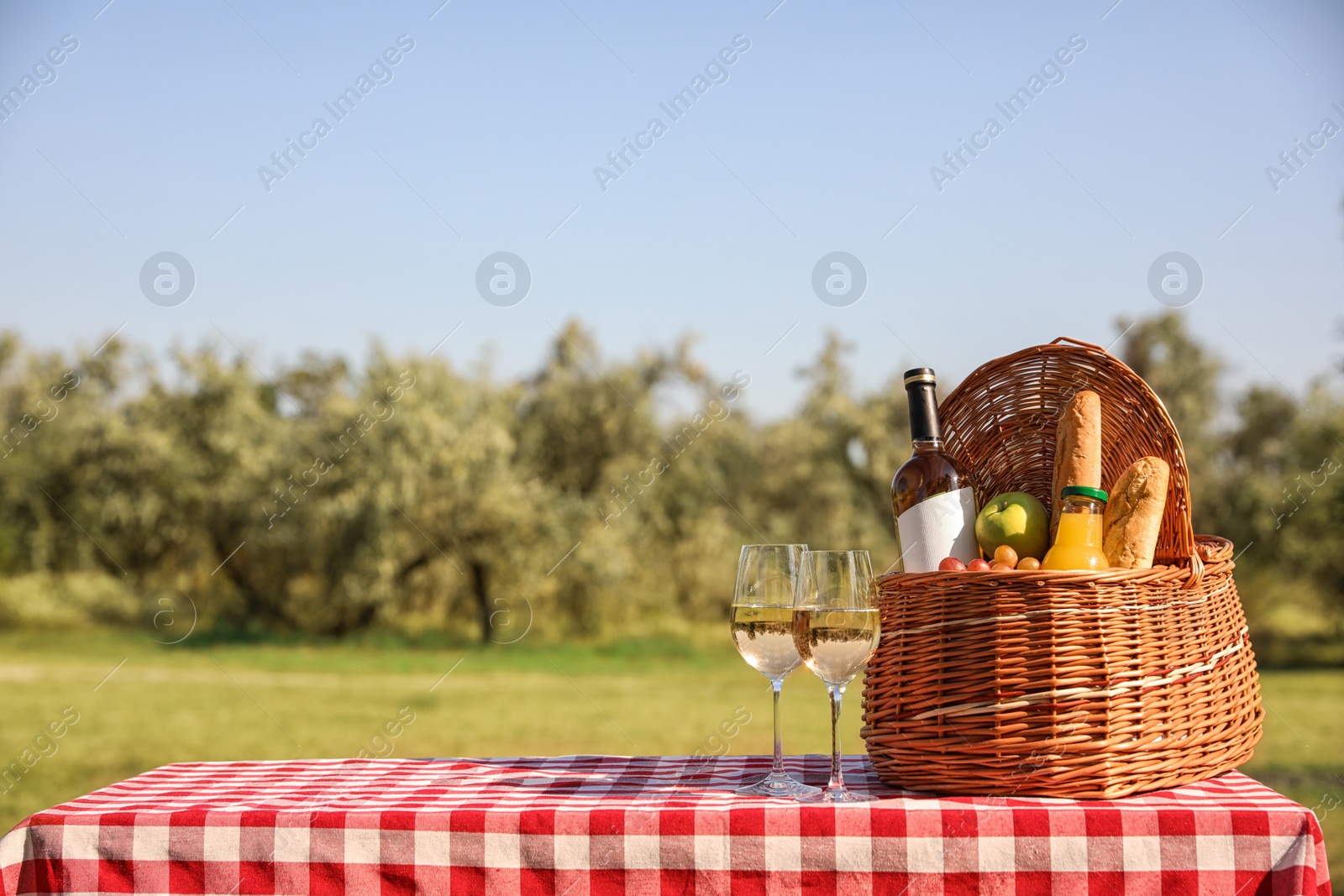 Photo of Wicker picnic basket with wine and snacks on table in park. Space for text