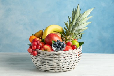 Assortment of fresh exotic fruits in wicker bowl on white wooden table against light blue background