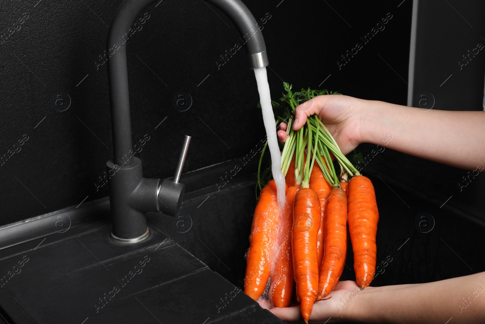 Photo of Woman washing fresh ripe juicy carrots under tap water in sink, closeup