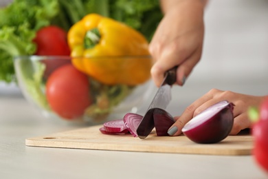 Young woman cutting onion at table, closeup