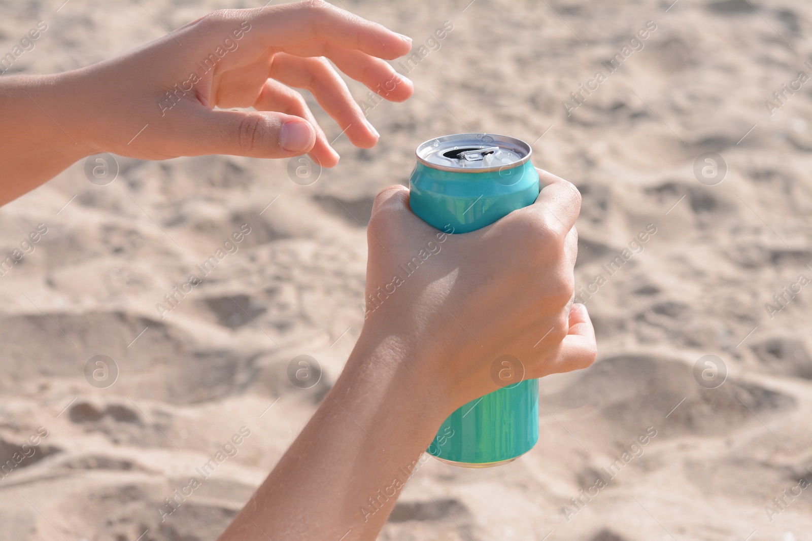 Photo of Woman holding aluminum can with beverage on sand, closeup