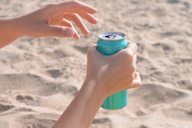 Photo of Woman holding aluminum can with beverage on sand, closeup