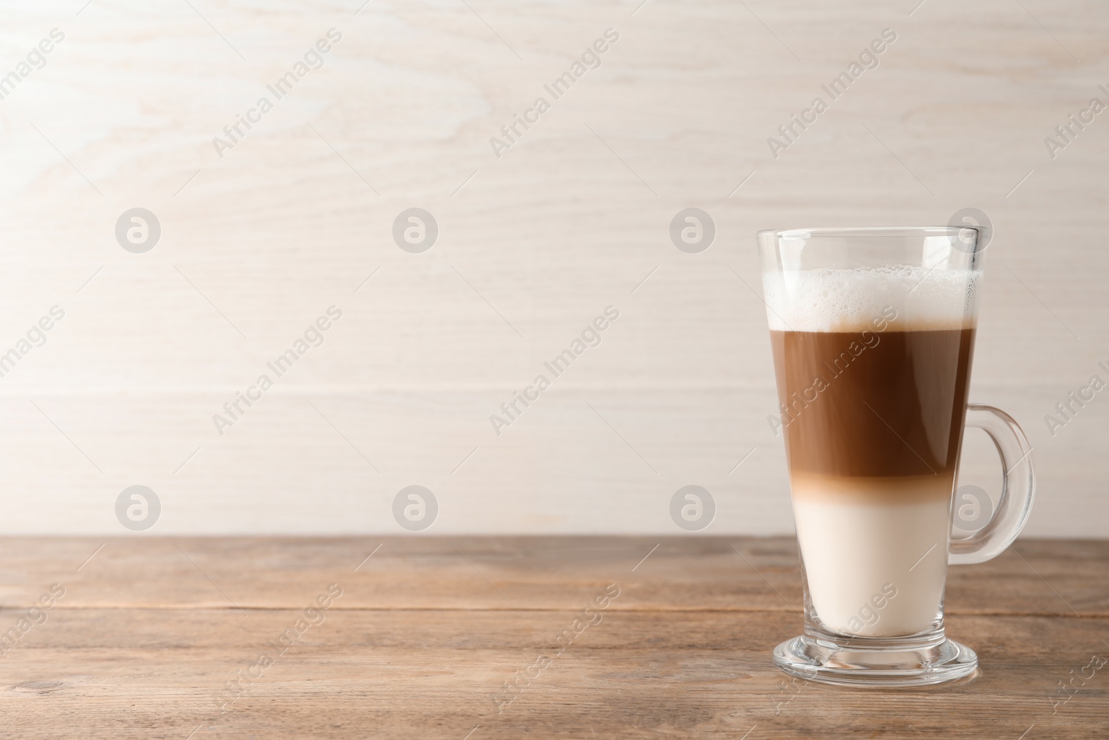 Photo of Hot coffee with milk in glass cup on wooden table. Space for text