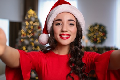 Beautiful woman in Santa hat taking selfie at home. Christmas celebration