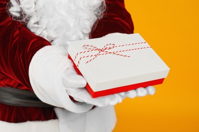 Santa Claus holding Christmas gift on yellow background, closeup