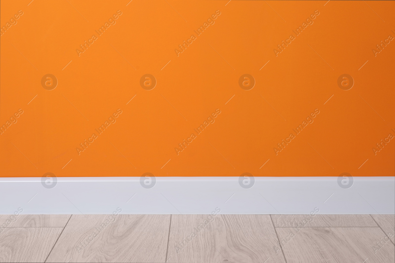 Photo of White plinth on laminated floor near orange wall indoors