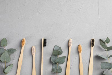 Many different bamboo toothbrushes and eucalyptus branches on light grey table, flat lay. Space for text