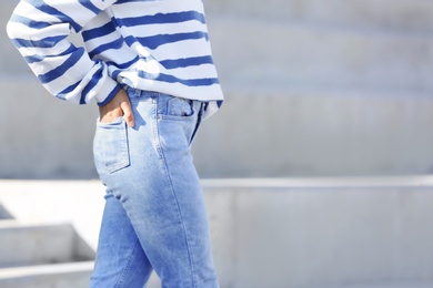 Photo of Young hipster woman in stylish jeans standing near stairs outdoors