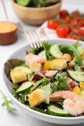 Delicious salad with croutons, cucumber and shrimp served on white tiled table, closeup