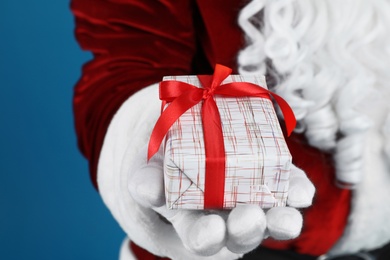 Santa Claus holding Christmas gift on blue background, closeup
