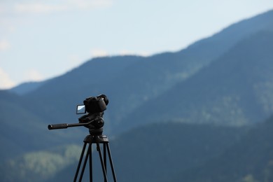 Photo of Tripod with modern camera in mountains. Space for text