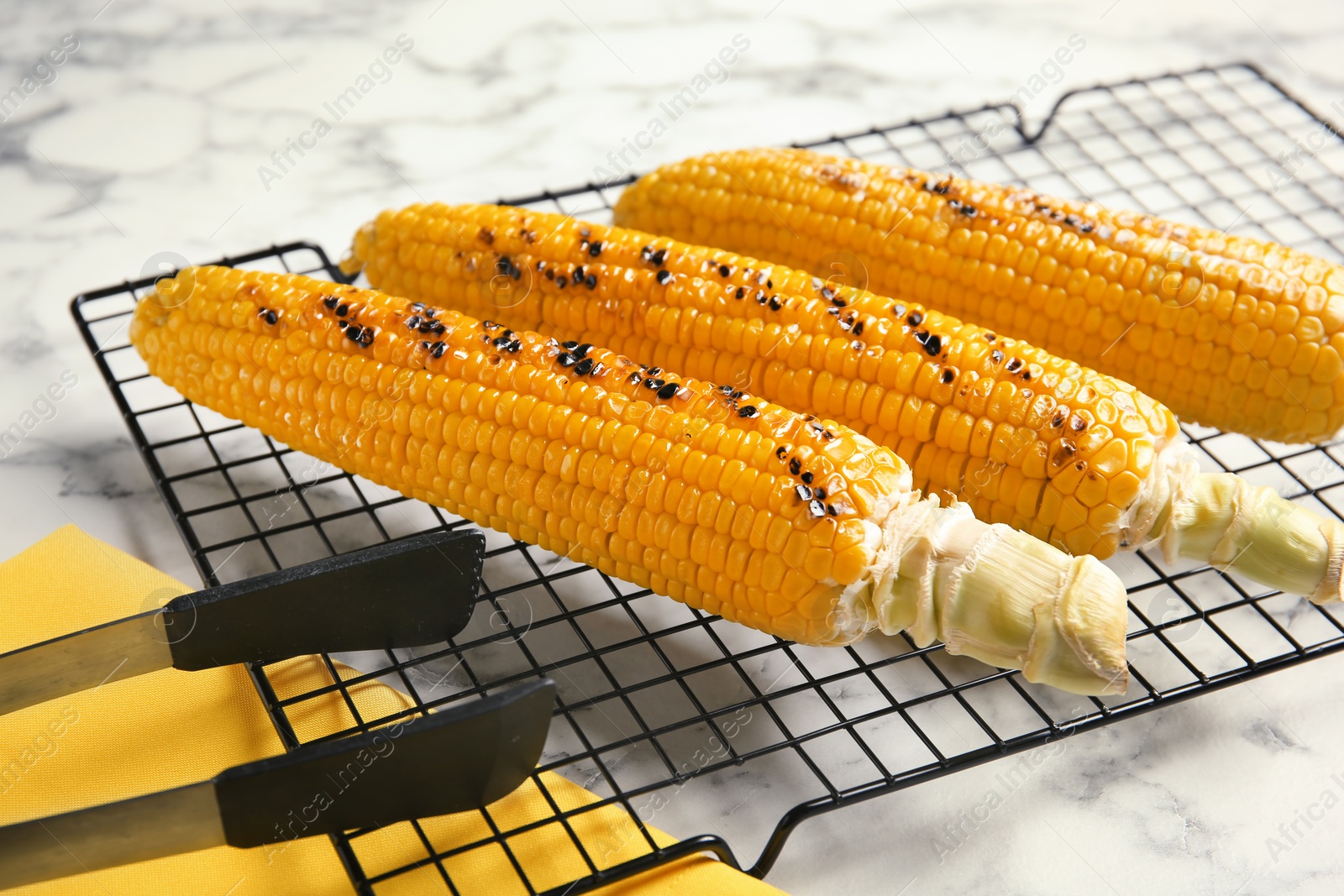 Photo of Cooling rack with grilled corn cobs on marble background