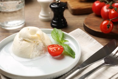 Photo of Delicious burrata cheese with basil and cut tomato served on wooden table, closeup