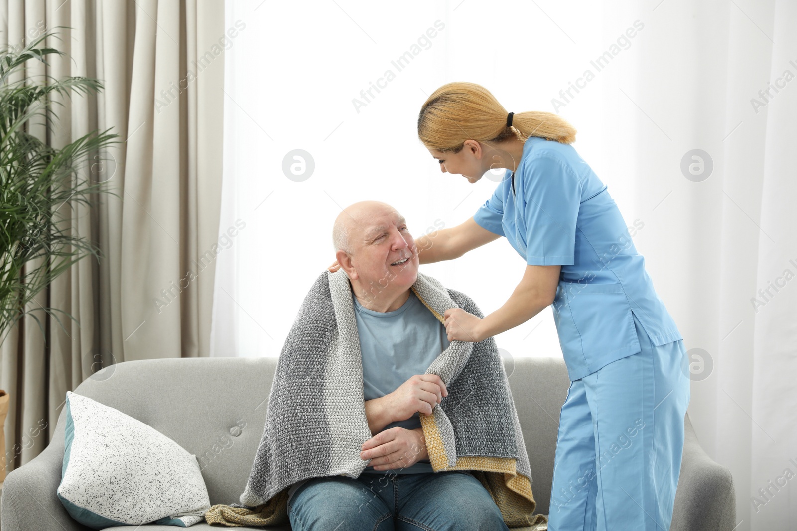 Photo of Nurse covering elderly man with blanket indoors. Assisting senior people