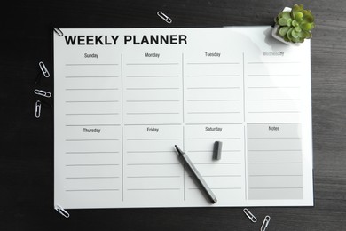 Photo of Timetable. Weekly planner, felt pen, houseplant and paper clips on black wooden table, top view