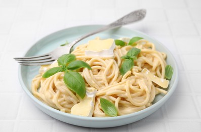 Photo of Delicious pasta with brie cheese, basil and fork on white tiled table, closeup