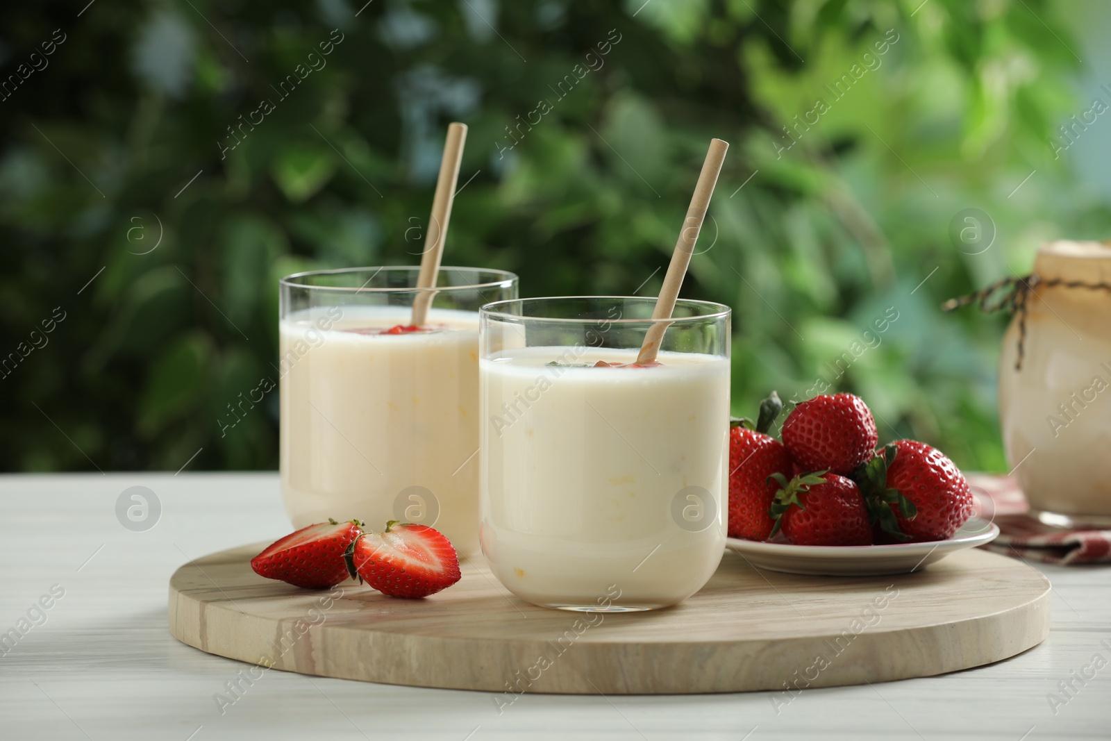 Photo of Tasty yogurt in glasses and strawberries on white wooden table outdoors