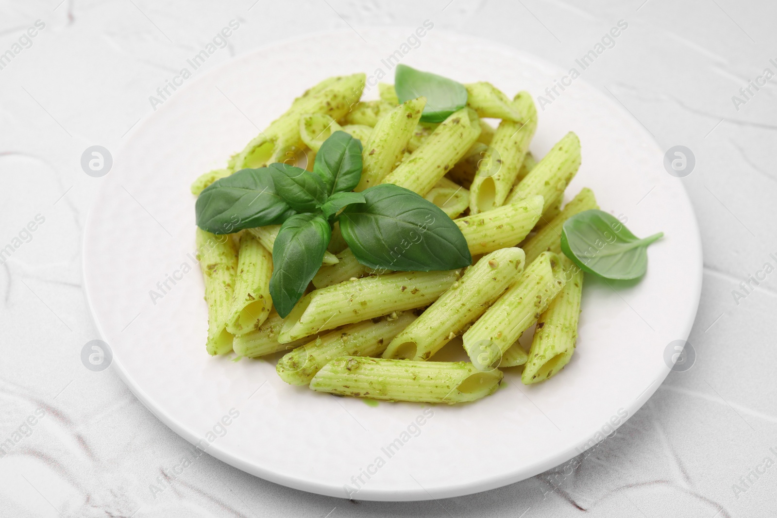 Photo of Delicious pasta with pesto sauce and basil on white textured table, closeup