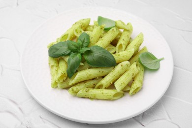 Delicious pasta with pesto sauce and basil on white textured table, closeup