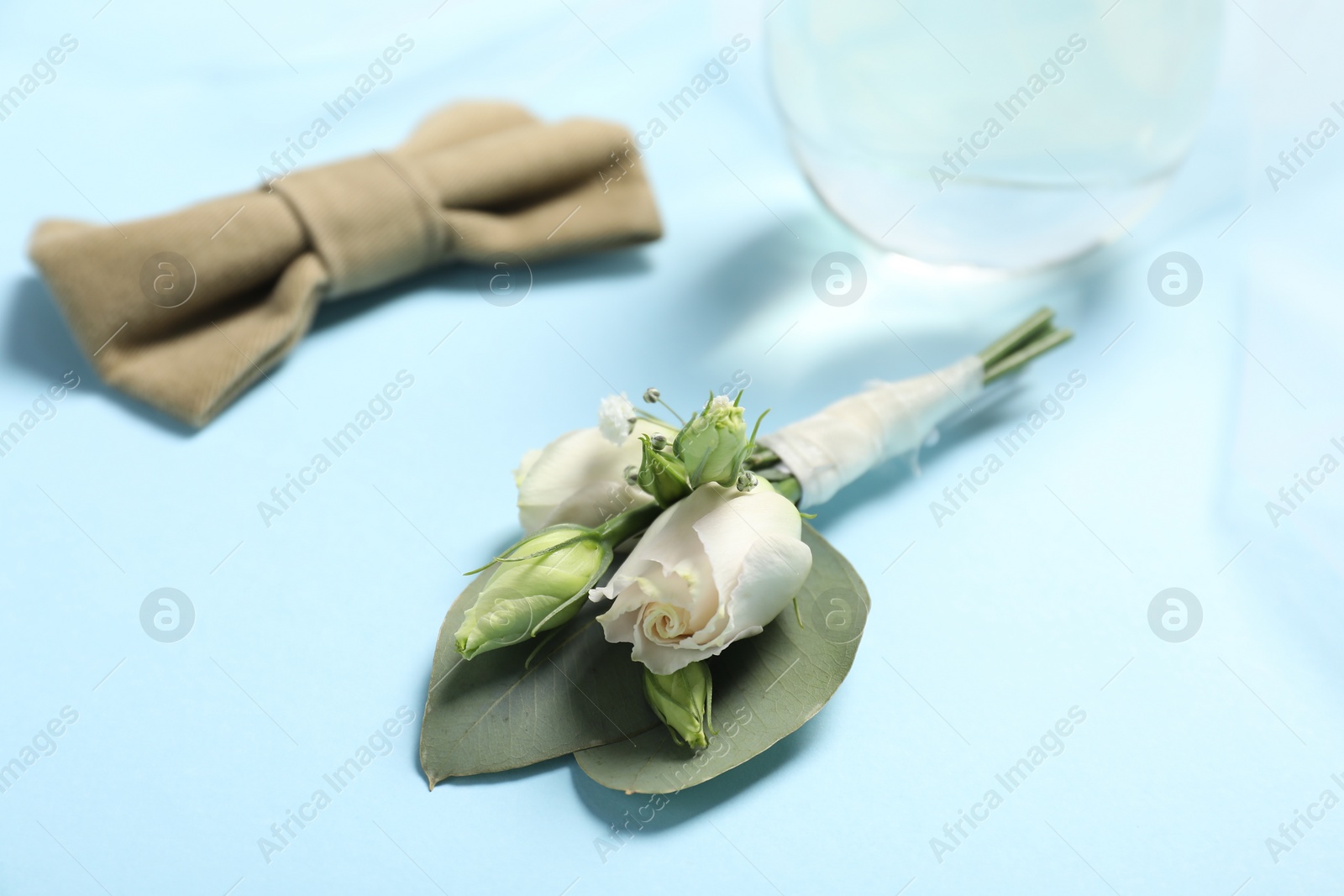 Photo of Wedding stuff. Stylish boutonniere and bow tie on light blue background, closeup