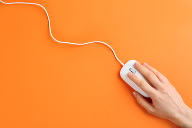Woman using modern wired optical mouse on orange background, top view
