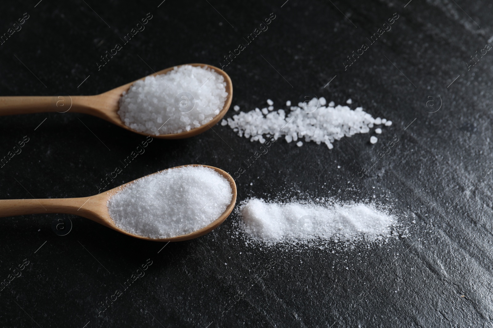 Photo of Organic salt in spoons on black table, closeup