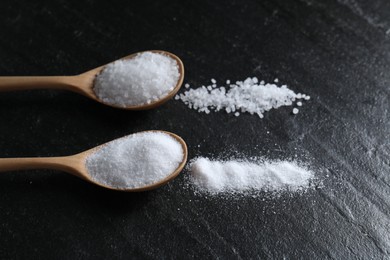 Photo of Organic salt in spoons on black table, closeup