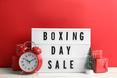 Composition with Boxing Day Sale sign and Christmas gifts on white table against red background