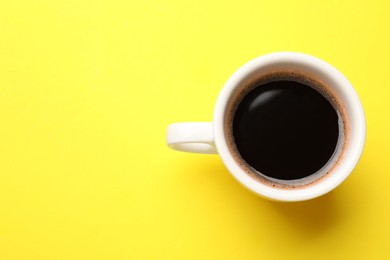 Photo of Fresh coffee in cup on yellow background, top view. Space for text