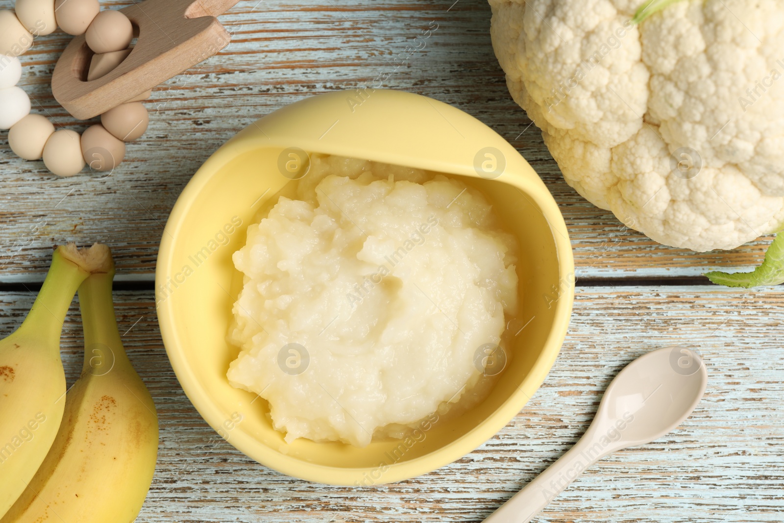 Photo of Baby food. Bowl with cauliflower puree and ingredients served on rustic wooden table, flat lay