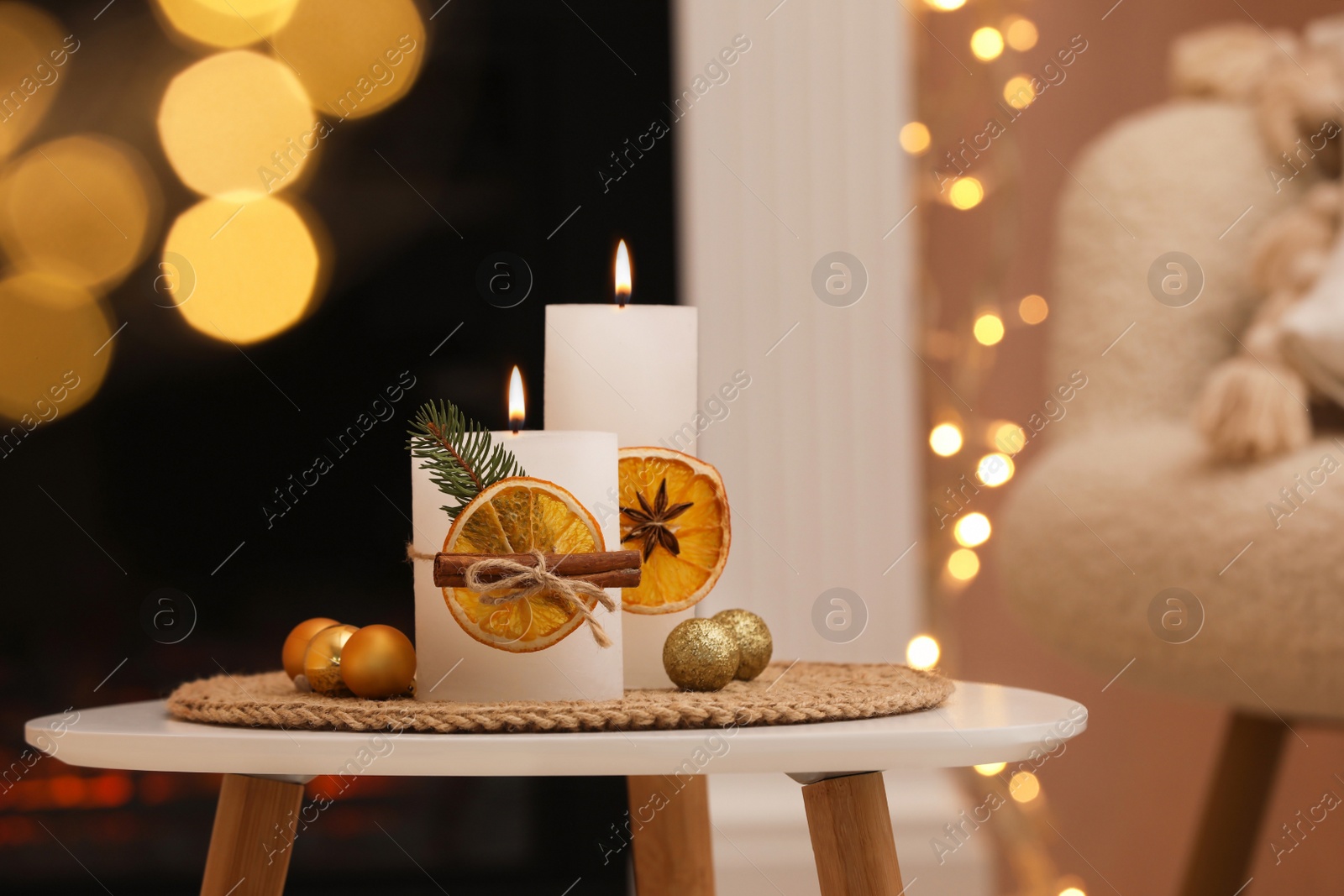 Photo of Beautiful candles decorated with dry orange slices and cinnamon sticks on white table indoors. Christmas atmosphere