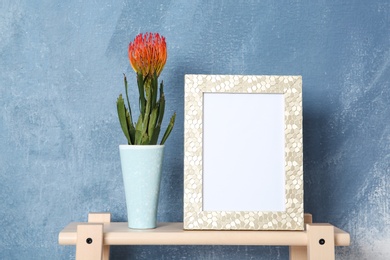 Photo of Blank frame and vase with flower on table near color wall. Mock up for design