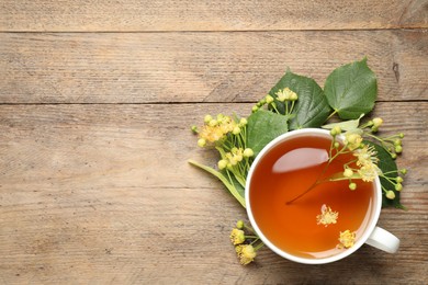 Cup of tea and linden blossom on wooden table, flat lay. Space for text