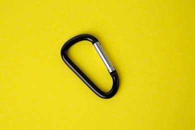 Photo of One black carabiner on yellow background, top view