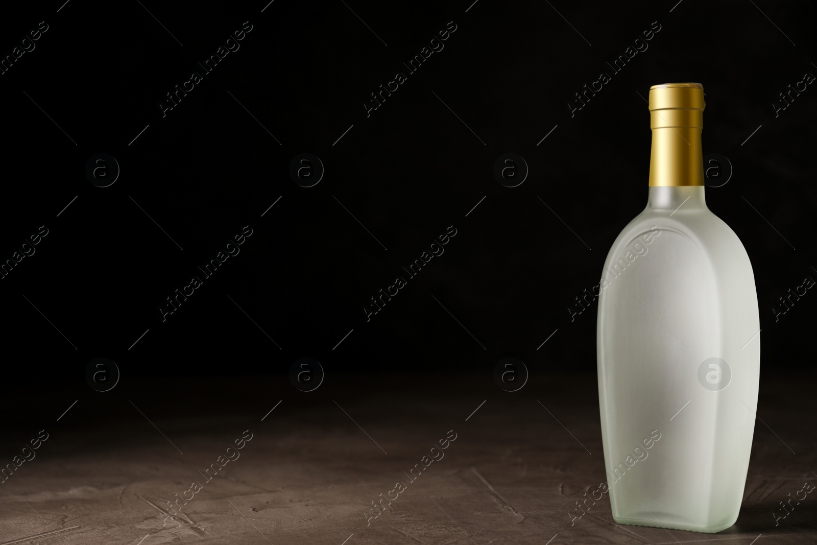 Photo of Bottle of vodka on grey table against black background. Space for text