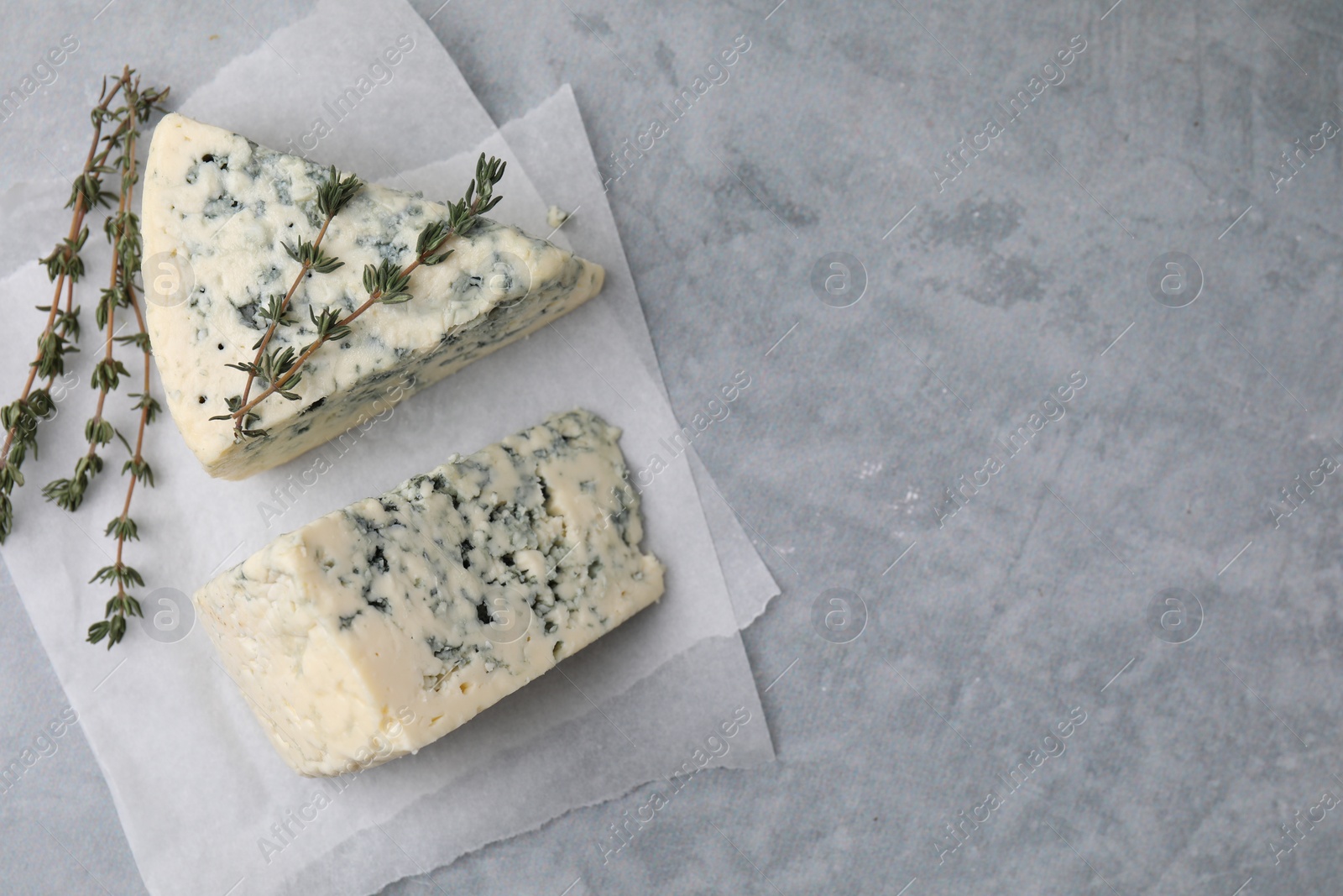 Photo of Tasty blue cheese with thyme on grey table, top view. Space for text