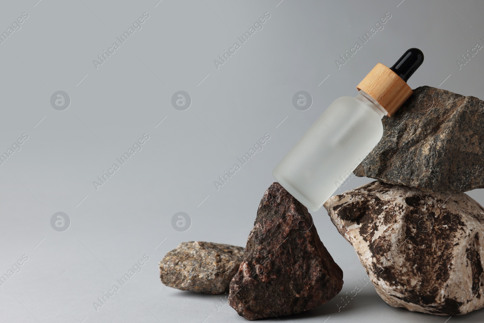 Photo of Glass bottle and stones on grey background, space for text