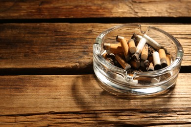 Photo of Glass ashtray with cigarette stubs on wooden table. Space for text