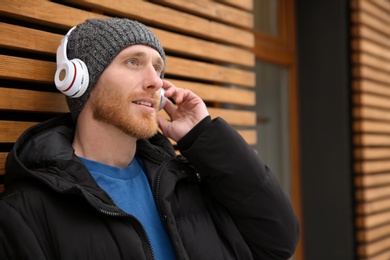 Photo of Young man listening to music with headphones near wooden wall. Space for text