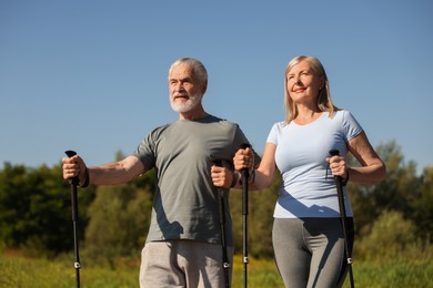 Photo of Senior couple with poles for Nordic walking outdoors on sunny day