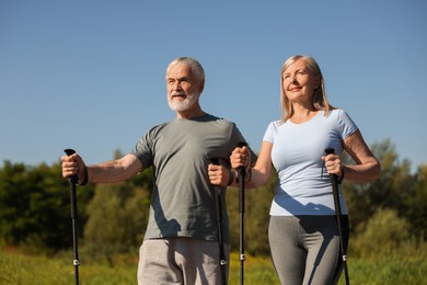 Senior couple with poles for Nordic walking outdoors on sunny day